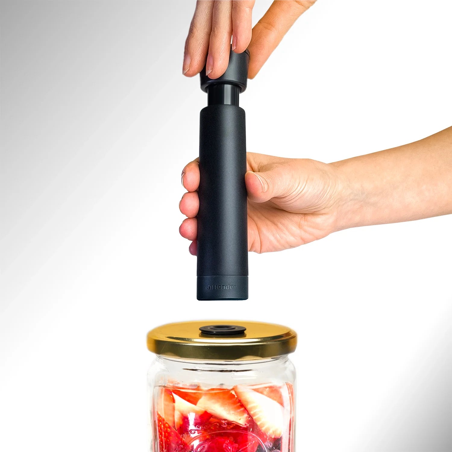 Hand holding an Airtender Vacuum Pump above a jar with a gold lid and Nanostopper on a white background