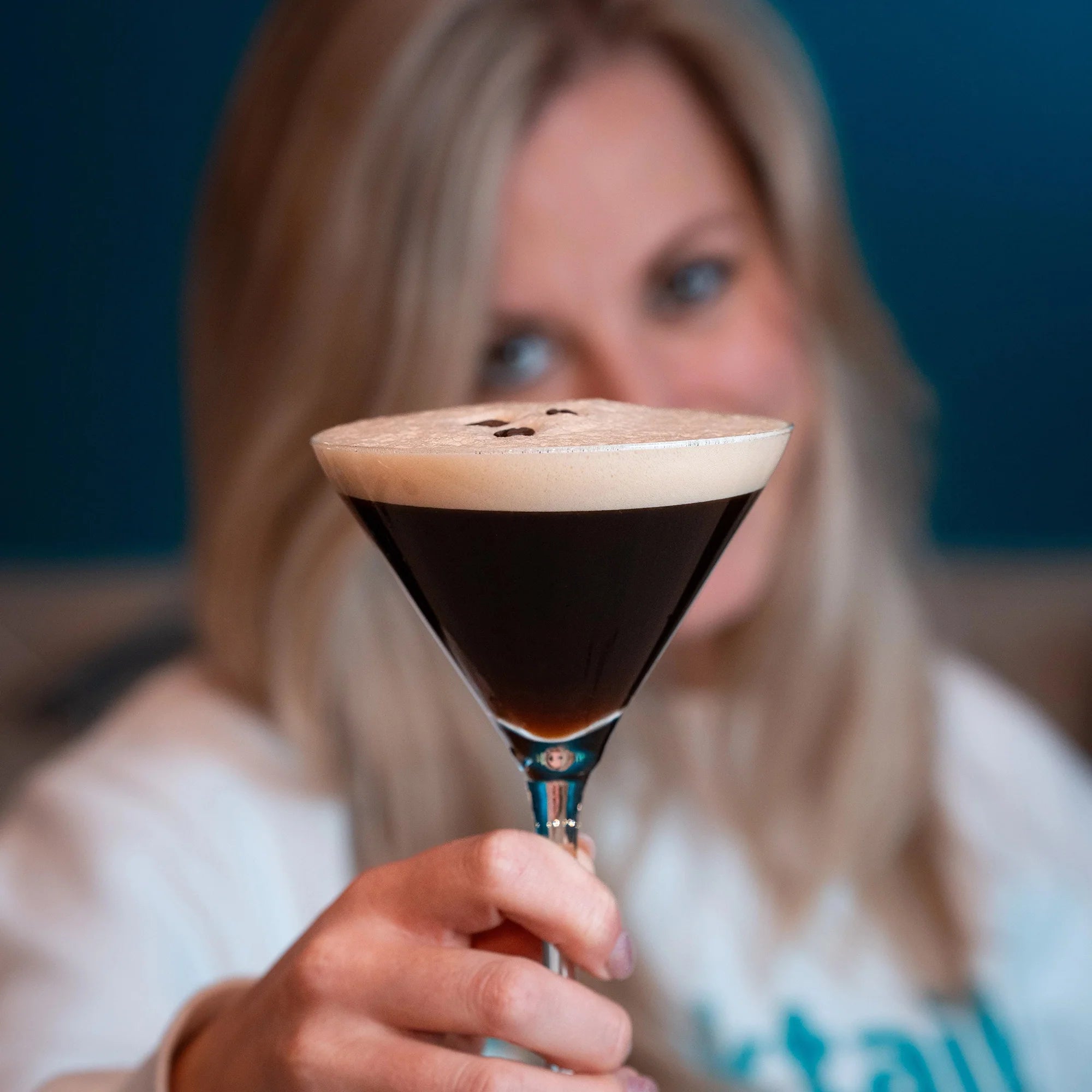 Person holding a martini glass with an espresso martini against a blurred background